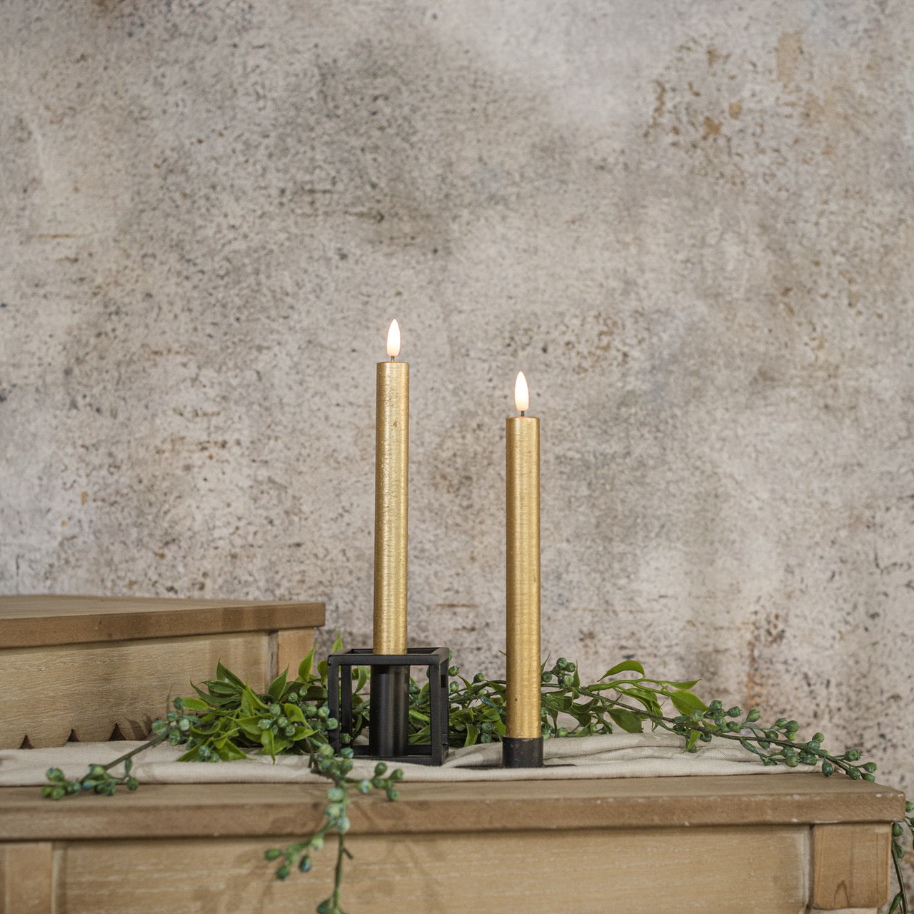 Set of two 9.5-inch 3D Flame Gold Taper Candles with a realistic flickering glow, displayed on a rustic wooden surface with greenery accents.