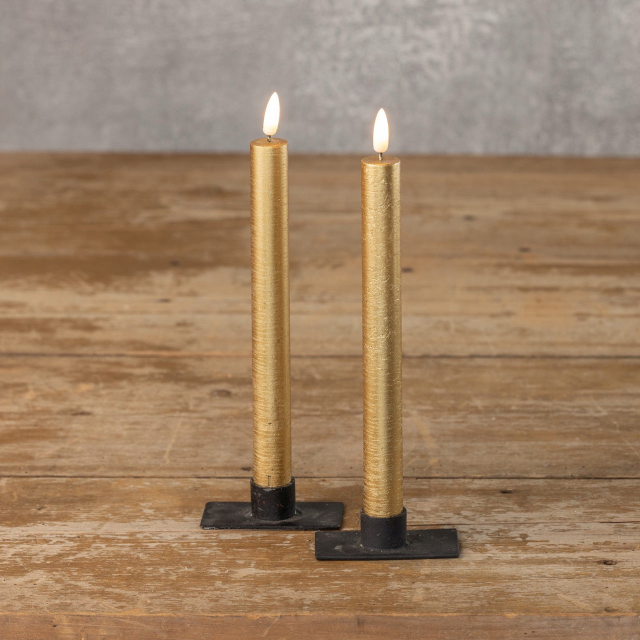 Pair of 9.5-inch 3D Flame Gold Taper Candles with a lifelike flickering flame, placed on a wooden table with black metal candle holders.