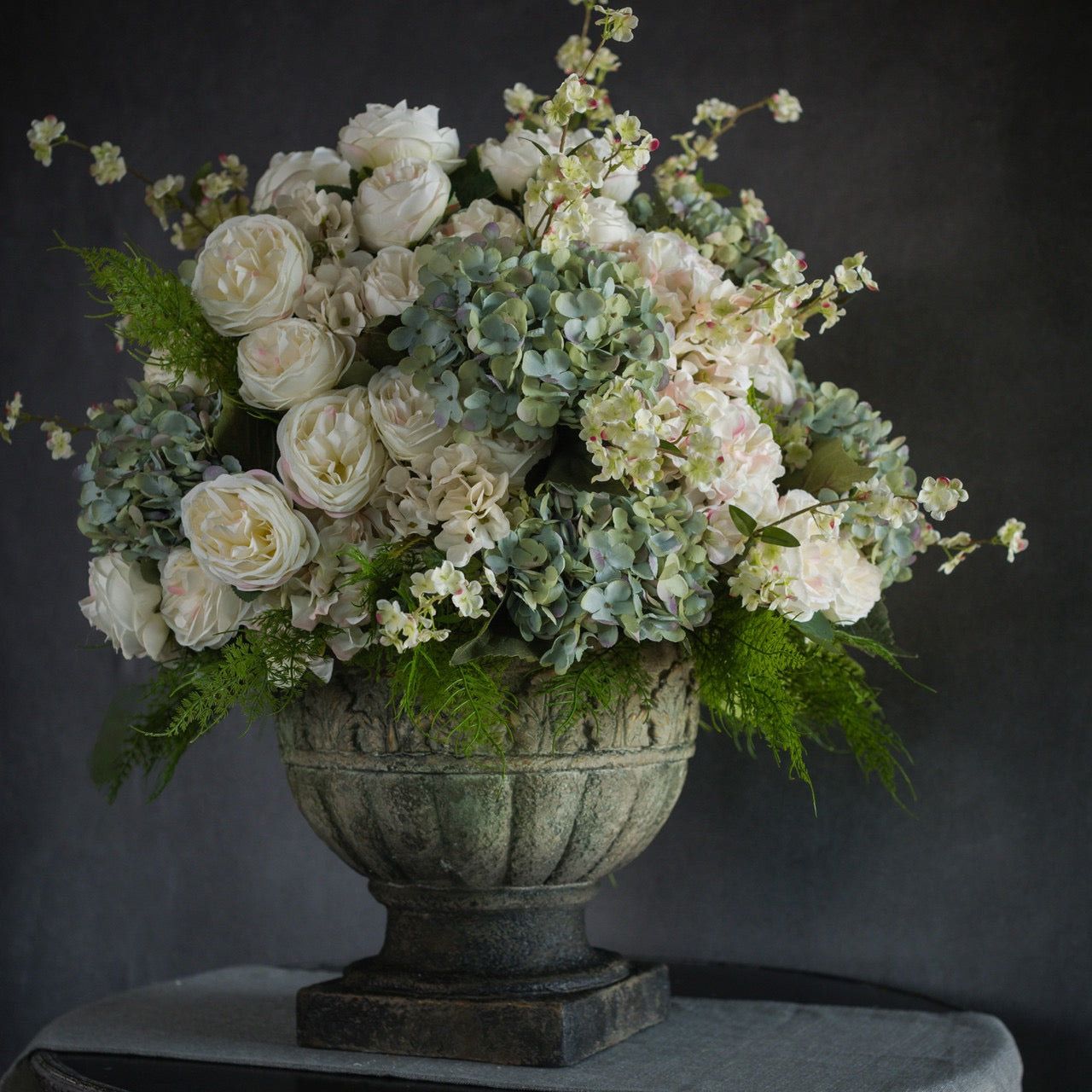 Luxurious floral arrangement featuring the Cream Rose Bush - 17.25" with hydrangeas and greenery in a classic urn. Perfect for elegant decor.