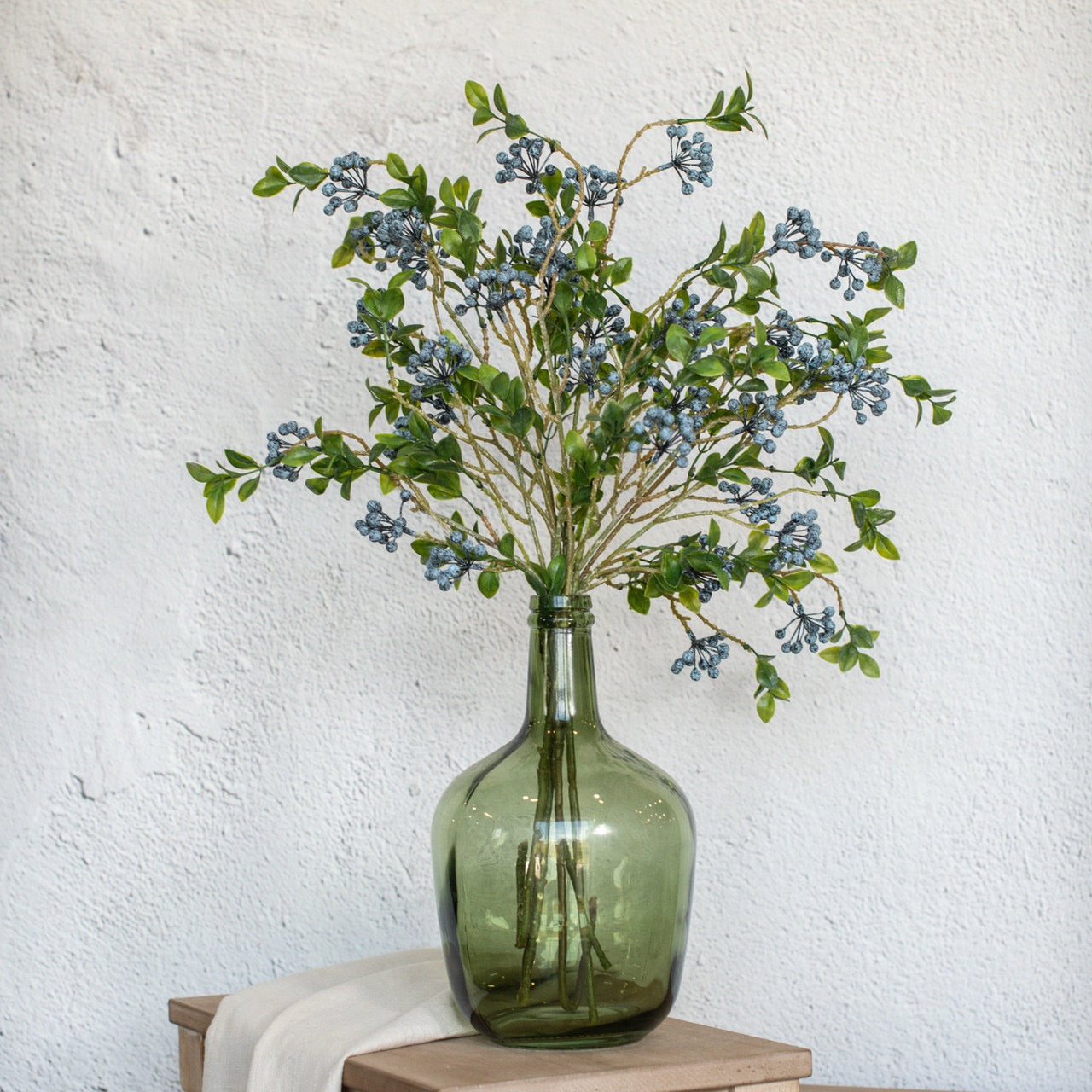 Decorative Blue Berry Foliage Spray arranged in a green glass vase, adding a fresh and modern botanical accent to any space.