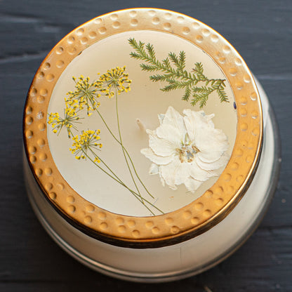 Close-up of Rosy Rings Honey Tobacco scented candle with a gold lid adorned with pressed flowers. A luxurious home fragrance with floral and honey notes.