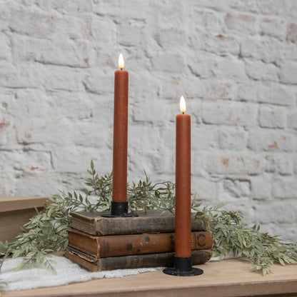 Set of two 3D flame bronze taper candles with a vintage design, placed on rustic books with greenery. Cozy home decor for a warm ambiance.