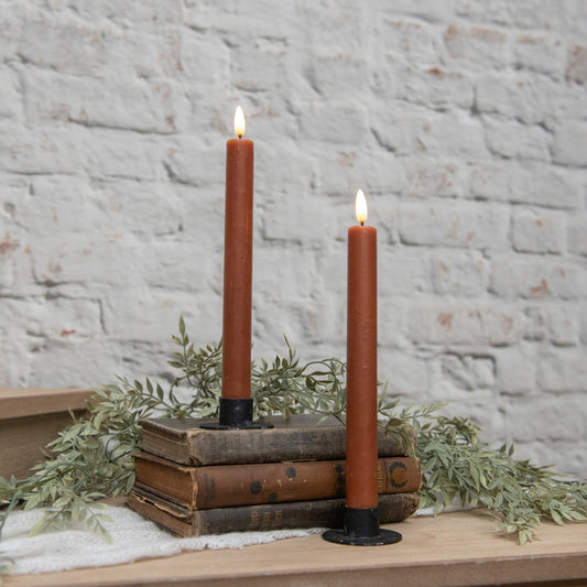 Set of two 3D flame bronze taper candles with a vintage design, placed on rustic books with greenery. Cozy home decor for a warm ambiance.