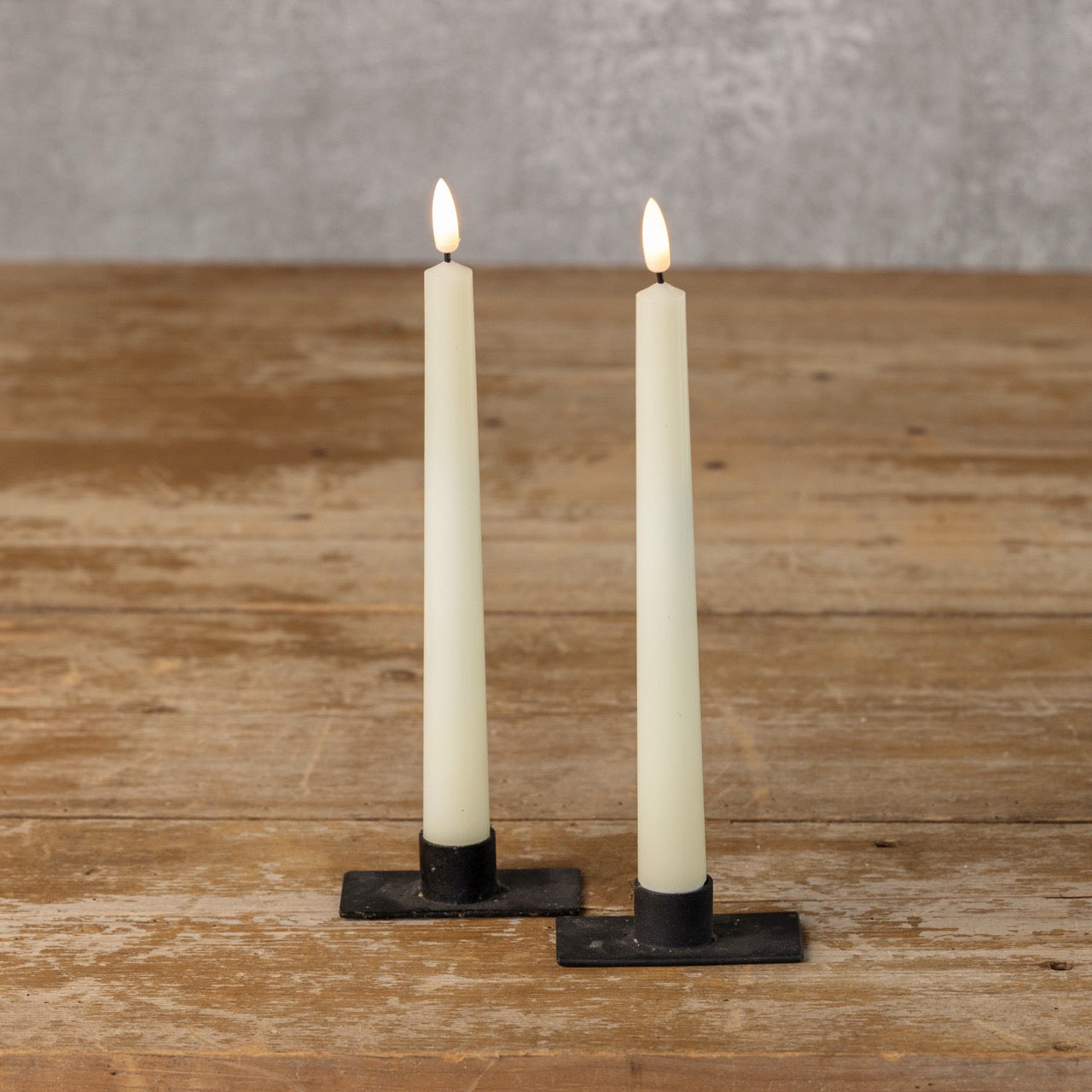 Pair of 9.5-inch cream taper candles with realistic 3D flame effect, standing in black holders on a rustic wooden table for a warm, inviting glow.