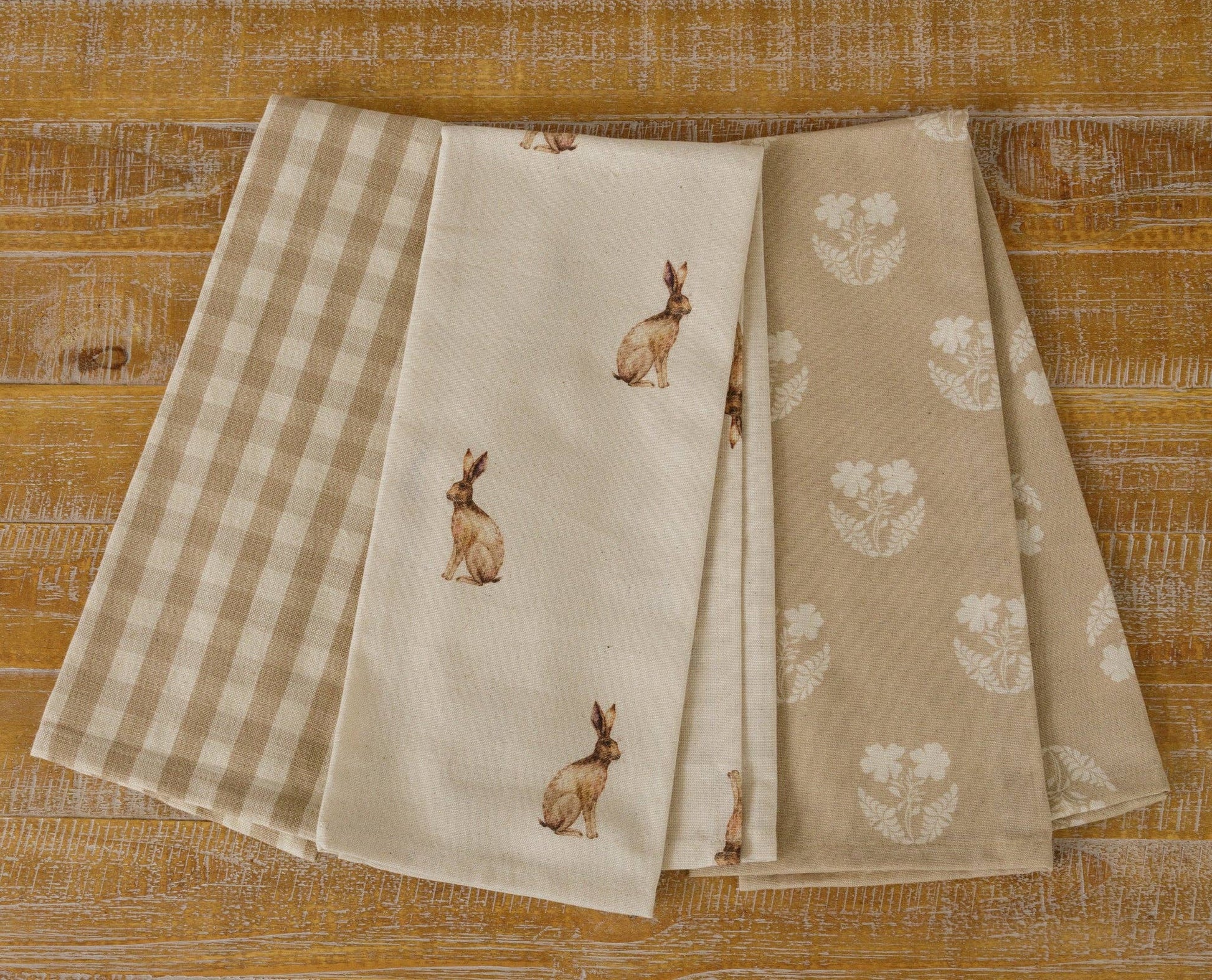 Set of 3 cotton tea towels featuring a rabbit print, tan check, and floral design. Each towel measures 27'x17', perfect for kitchen use and decor.