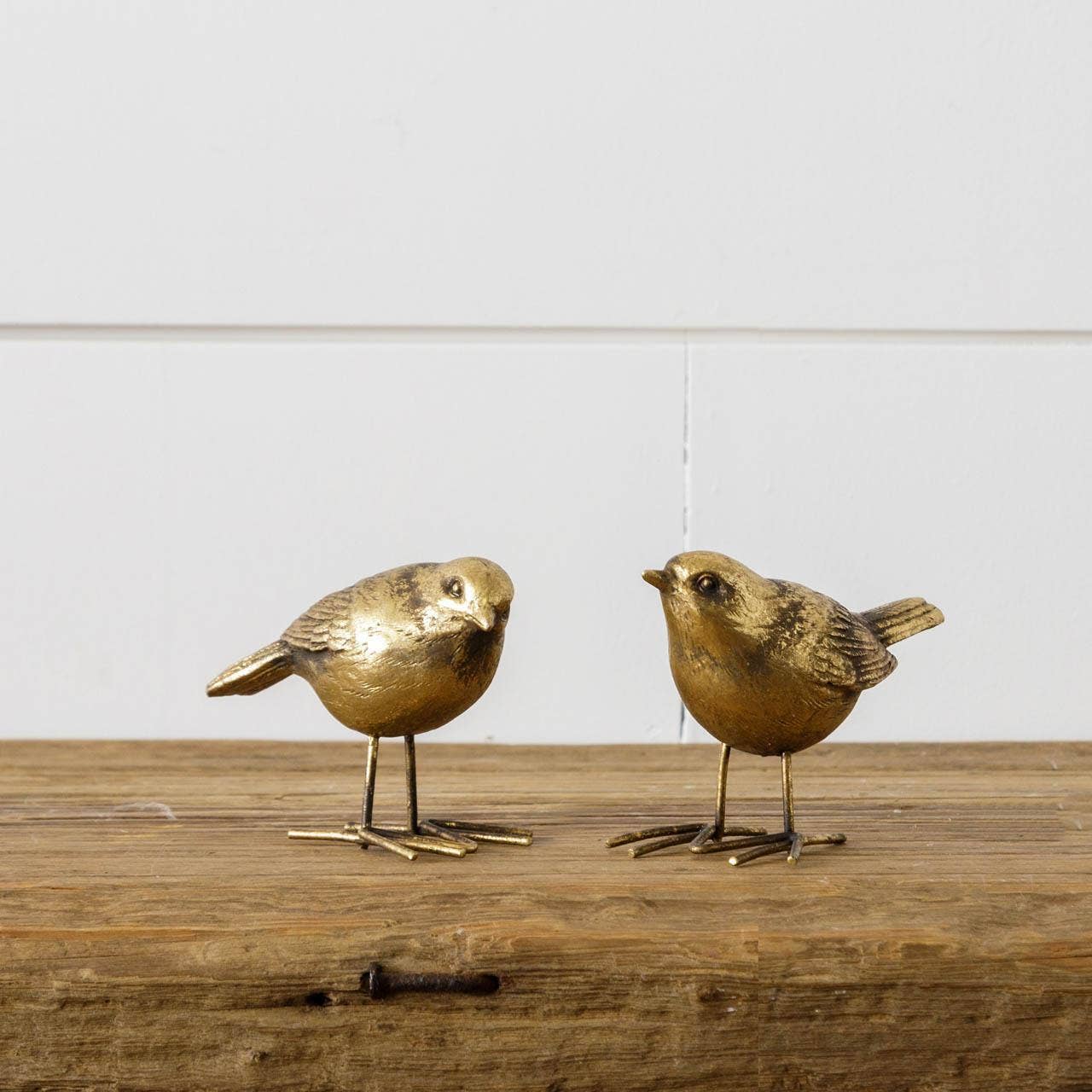 Pair of brass bird figurines with a rustic finish, placed on a wooden surface. A charming addition to home decor, blending nature-inspired elegance.